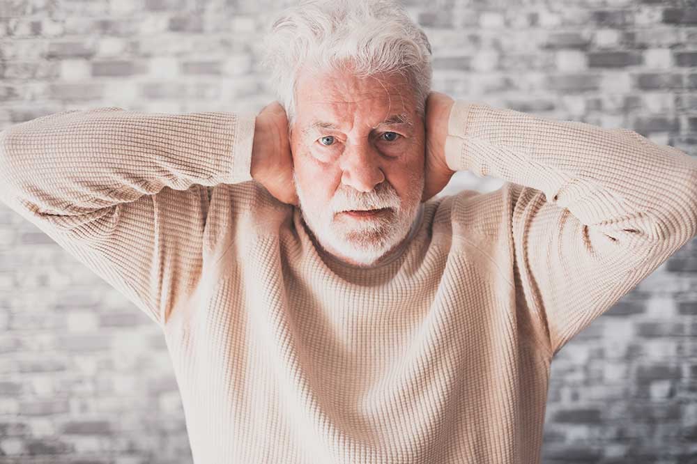 Older man covering both ears over a clogged, muffled feeling, a concern Livingston & Commerce Hearing Center sees in Hartland, MI
